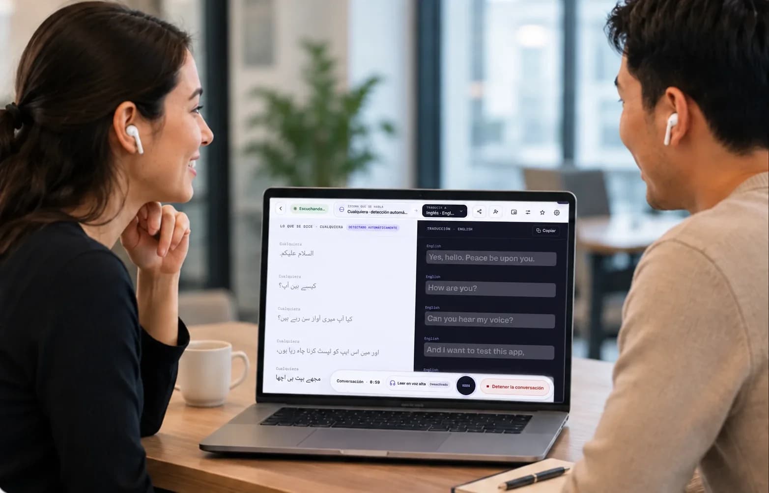 Dos personas conversan en una mesa de oficina, cada una con sus audífonos, mientras Mingle traduce su conversación en vivo en la computadora portátil que está entre ellas.